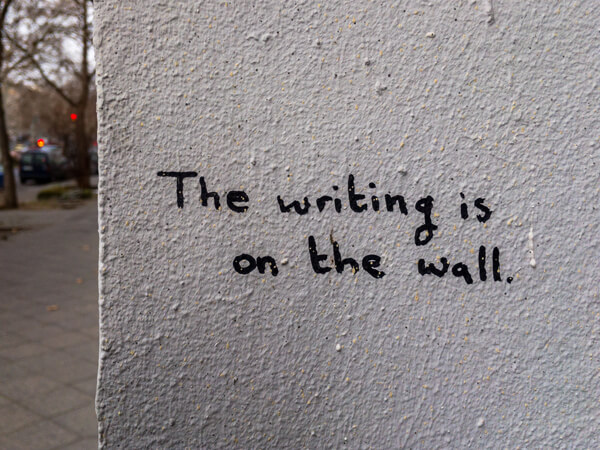 A white wall with grafitti that says 'the writing is on the wall