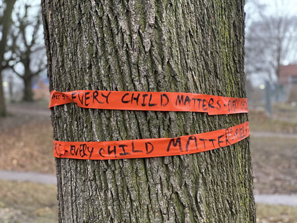 An orange ribbon wrapped about a tree that reads 'Every Child Matters'